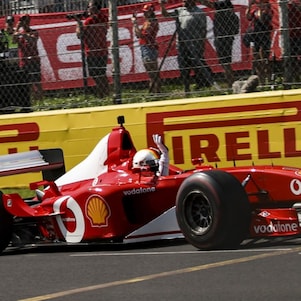 Side view of the Ferrari F2002 car on track at Monza, with the driver raising a hand towards spectators.