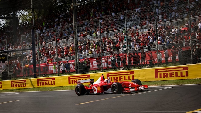Ferrari F2002 car driving around the Monza circuit, photographed from a distance with trackside barriers in the background.