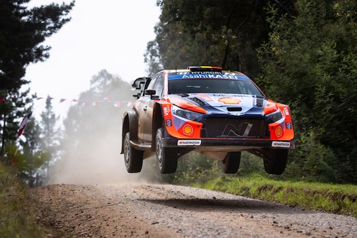 Spectators photograph a Hyundai rally car driving on a dusty road.