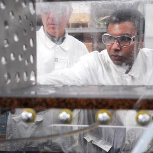 A group of people in white coats watching machinery close