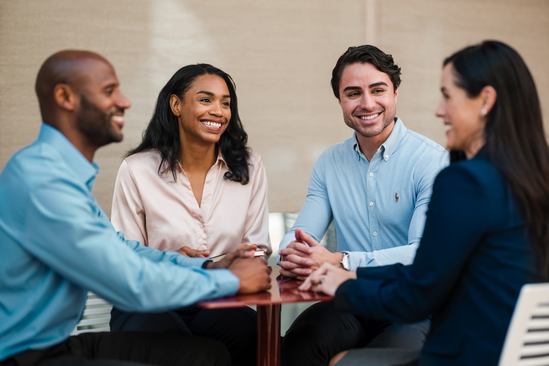 A group of people standing together indoors against a neutral beige background.