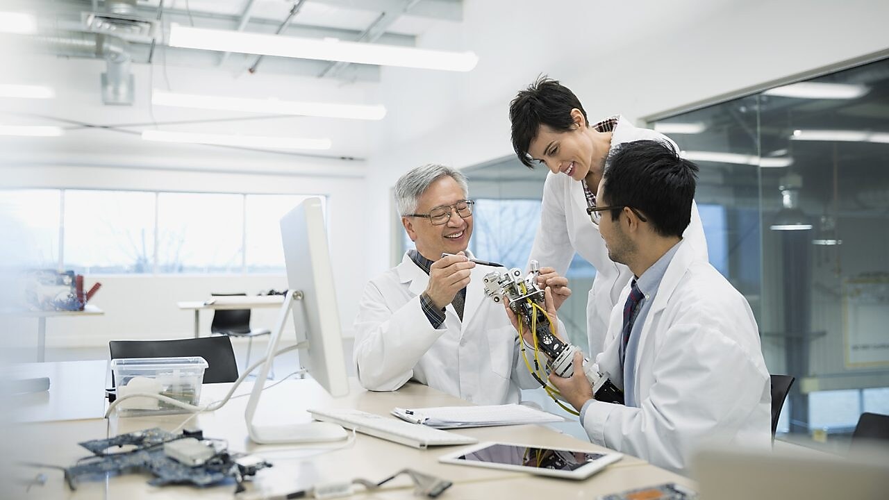 Three people wearing white lab coats talking